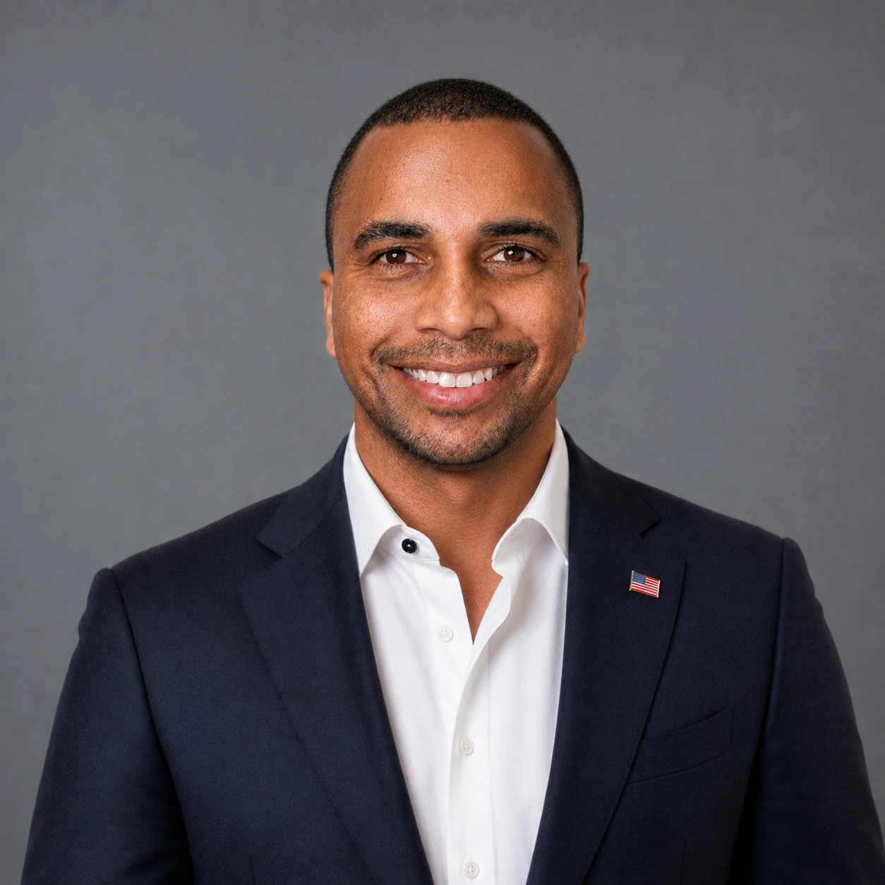 Nathaniel Smith III in a navy jacket and open-collar white shirt with an American flag lapel pin against a gray background